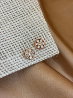 Rose gold earrings with clear stones on a textured beige fabric background