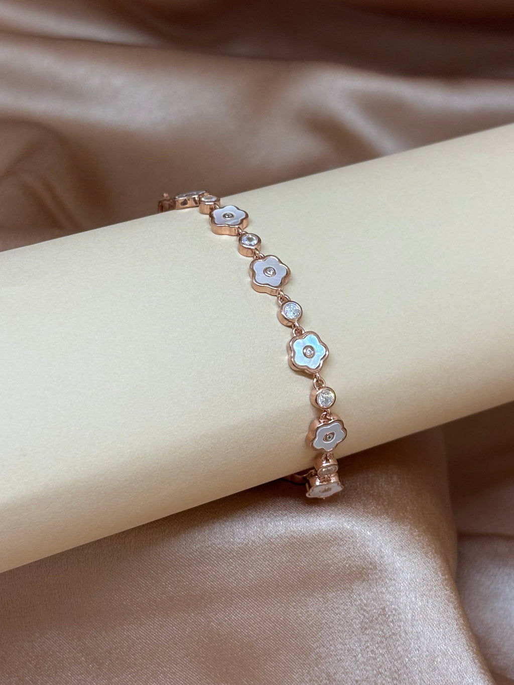 Rose gold bracelet with floral designs on a beige ribbon against a satin background