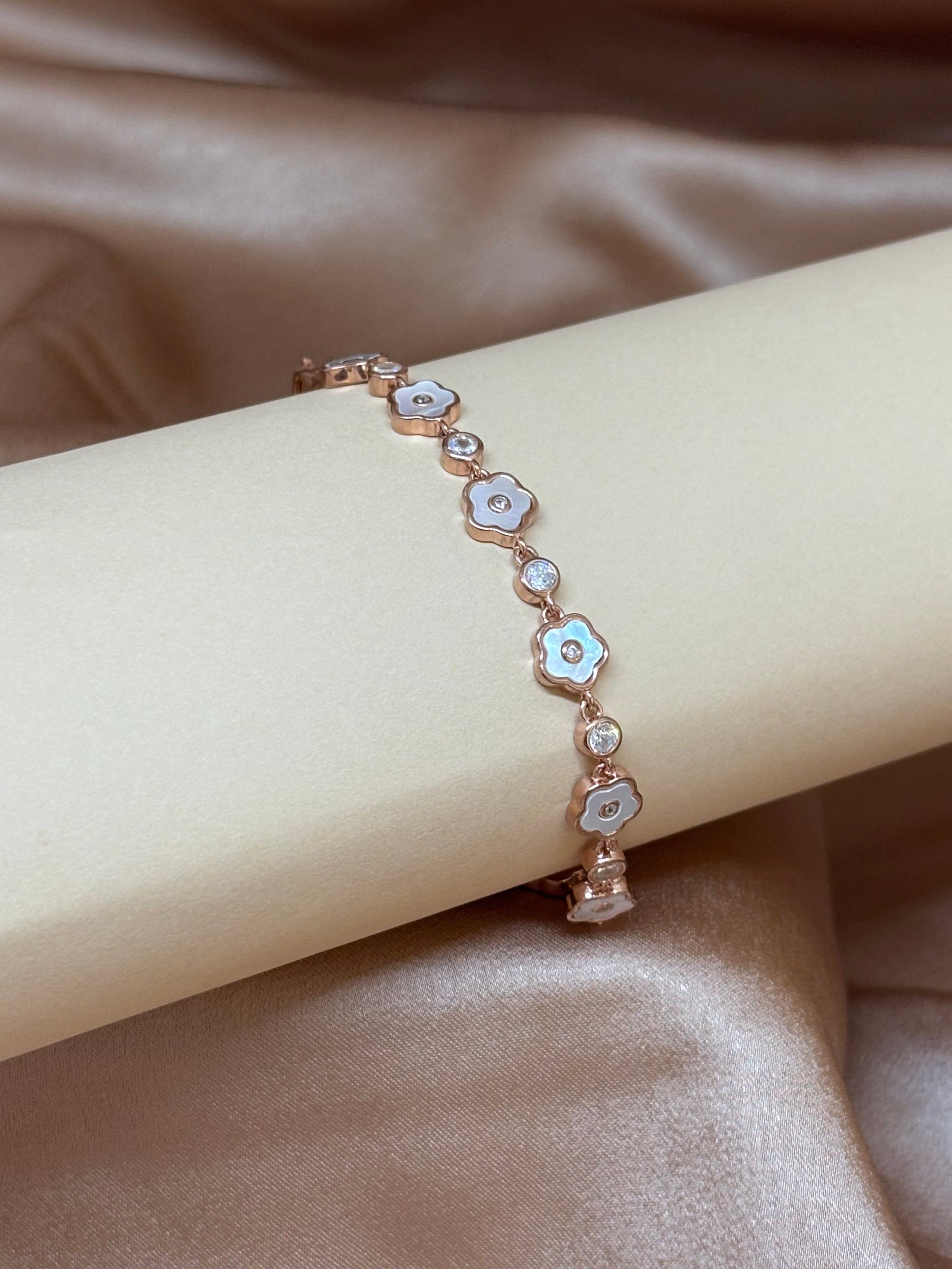 Rose gold bracelet with floral designs on a beige ribbon against a satin background