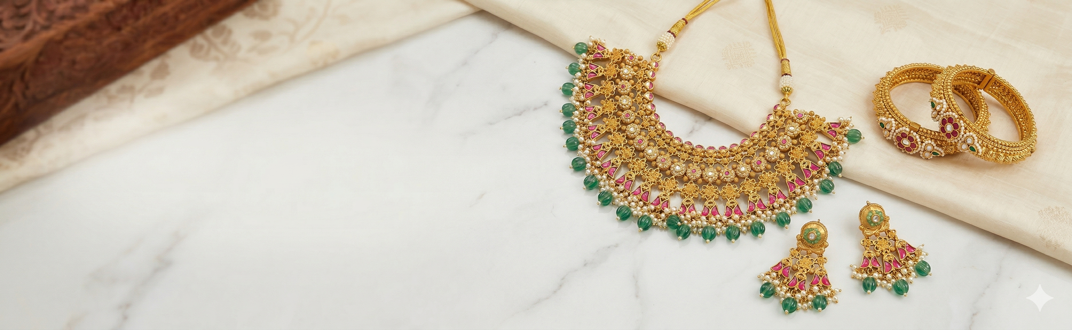 Gold necklace with green gemstones, gold bangles, and earrings on a marble surface.